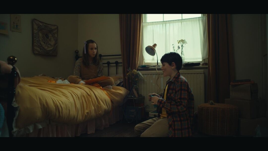 A woman and a boy sitting in a cozy, dimly lit bedroom with natural light from a window, engaging in.
