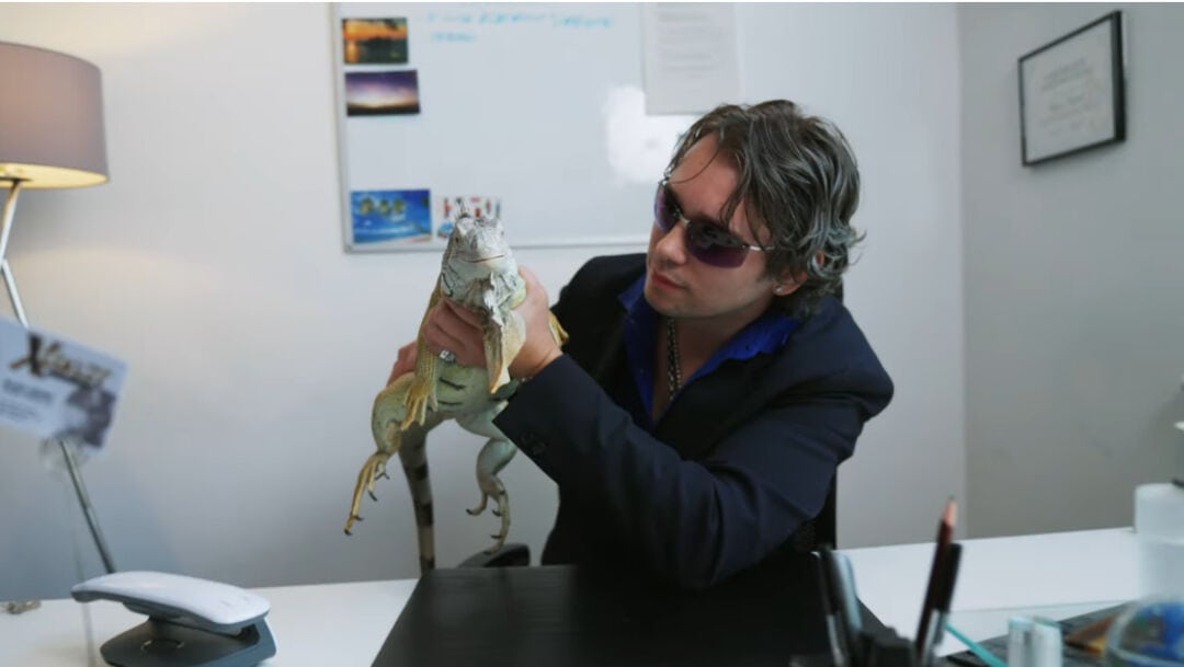 A man in sunglasses holding a puppet crocodile in an office setting.